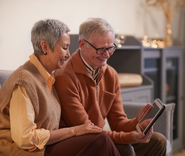 Seniorenpaar sitzt auf dem Sofa und hält ein Tablet in Händen